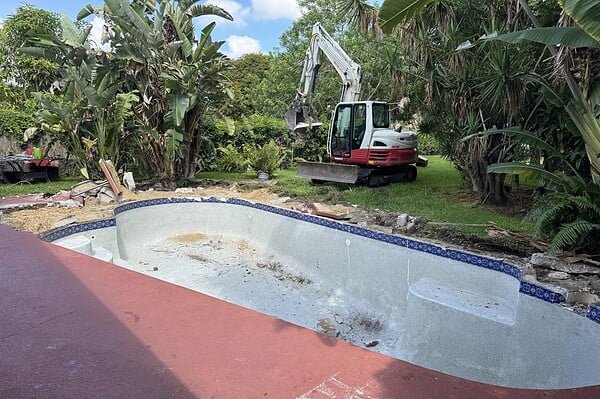 Concrete swimming pool before demolition in Royal Palm Beach, FL, with a Thum Co. excavator staged to begin removal