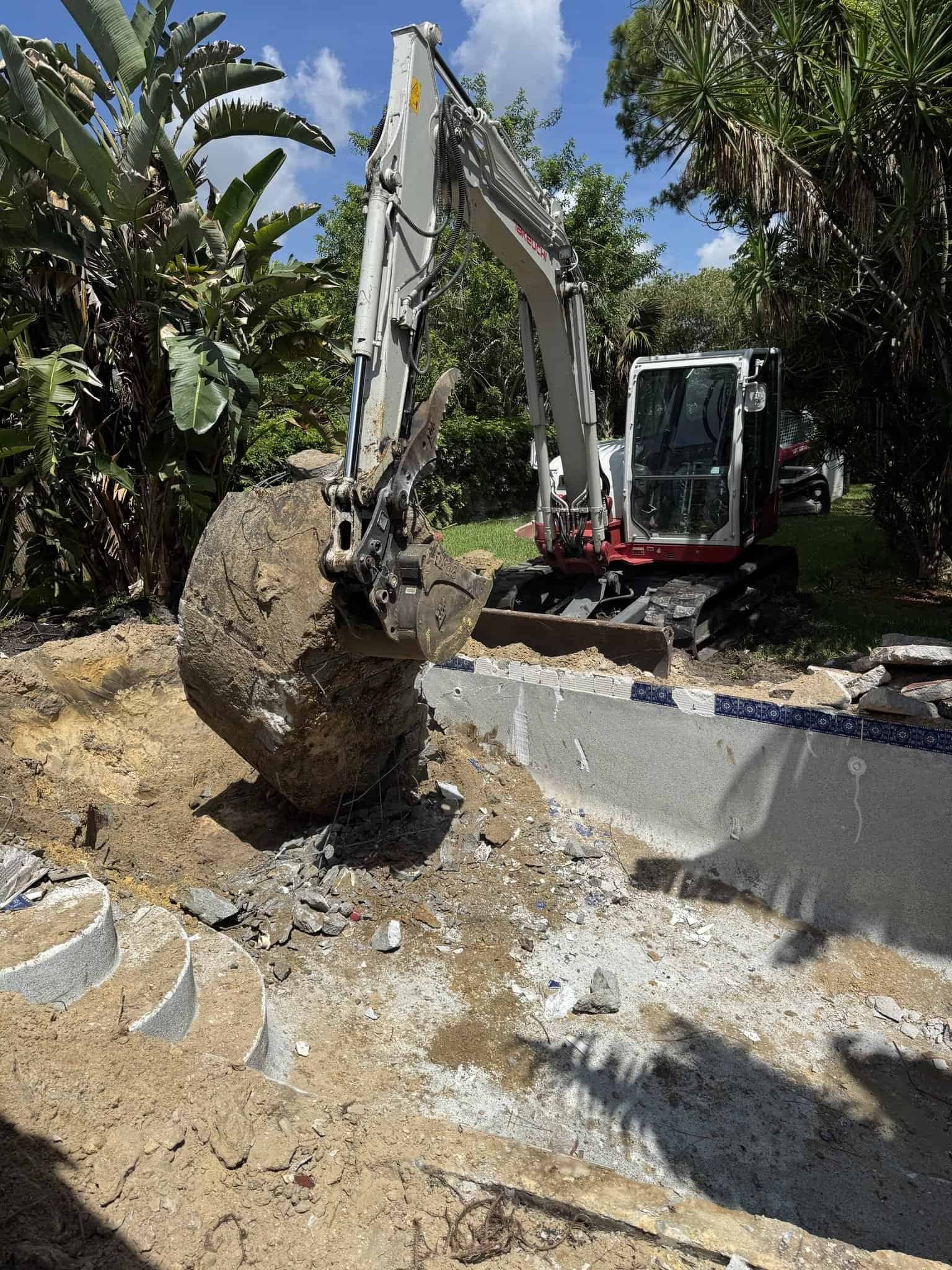 Excavator breaking up the concrete pool shell during swimming pool removal in Royal Palm Beach, FL
